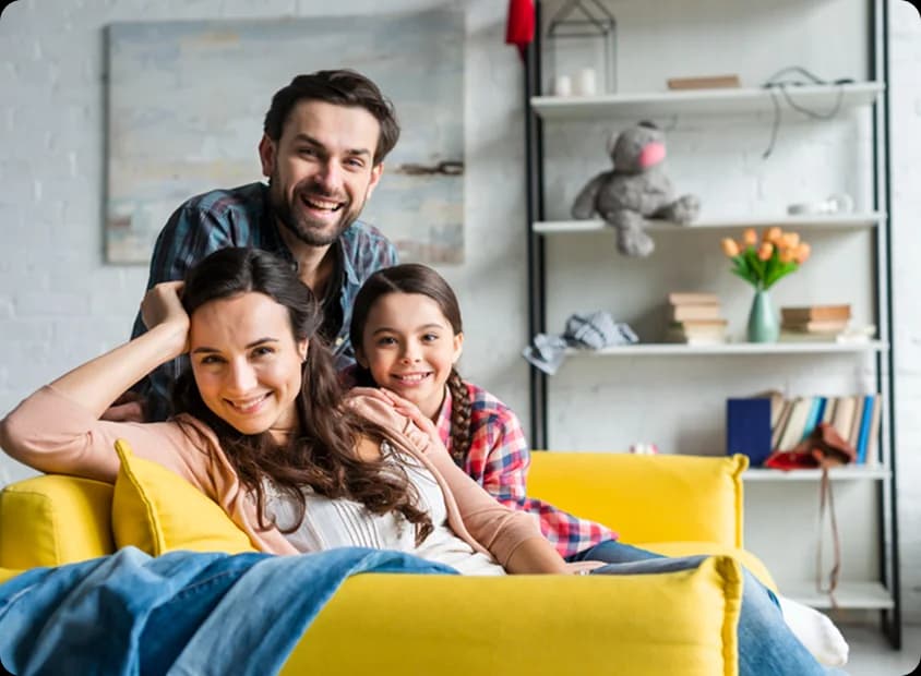 Happy family sitting together on a bright yellow sofa, smiling and looking at the viewer