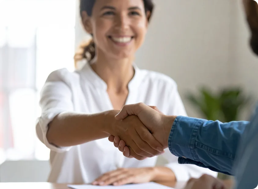 Two people shaking hands across a light-colored table, symbolizing trust and partnership